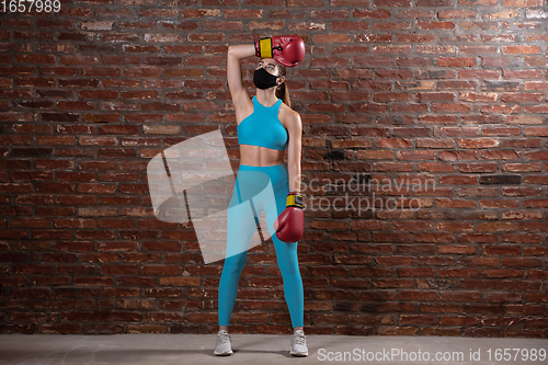 Image of Professional female athlete training on brick wall background wearing face mask. Sport during quarantine