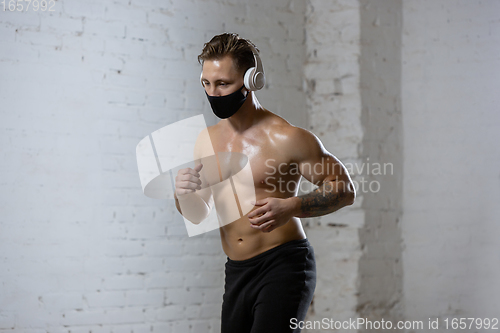 Image of Professional male athlete training on brick wall background wearing face mask. Sport during quarantine