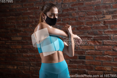 Image of Professional female athlete training on brick wall background wearing face mask. Sport during quarantine