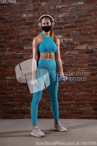 Image of Professional female athlete training on brick wall background wearing face mask. Sport during quarantine