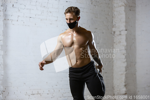 Image of Professional male athlete training on brick wall background wearing face mask. Sport during quarantine