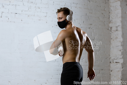 Image of Professional male athlete training on brick wall background wearing face mask. Sport during quarantine