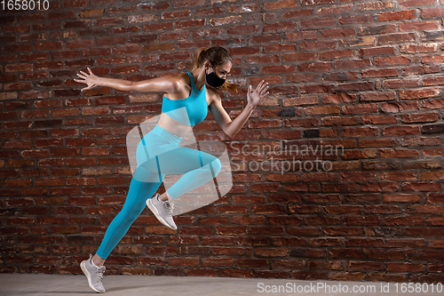 Image of Professional female athlete training on brick wall background wearing face mask. Sport during quarantine