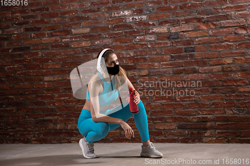 Image of Professional female athlete training on brick wall background wearing face mask. Sport during quarantine