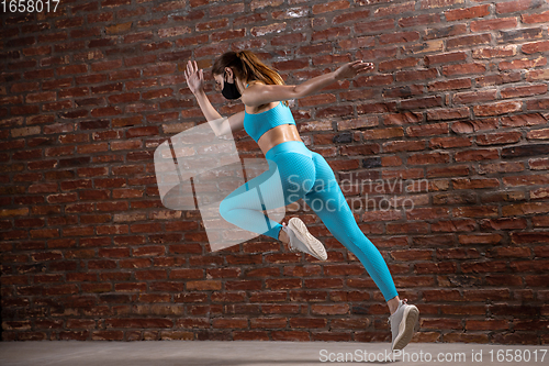 Image of Professional female athlete training on brick wall background wearing face mask. Sport during quarantine