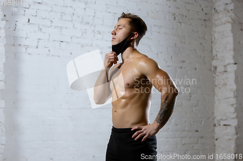 Image of Professional male athlete training on brick wall background wearing face mask. Sport during quarantine