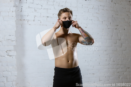 Image of Professional male athlete training on brick wall background wearing face mask. Sport during quarantine