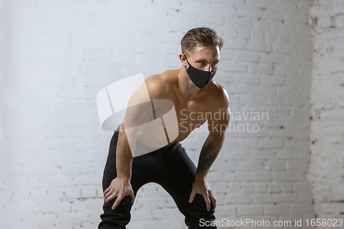 Image of Professional male athlete training on brick wall background wearing face mask. Sport during quarantine