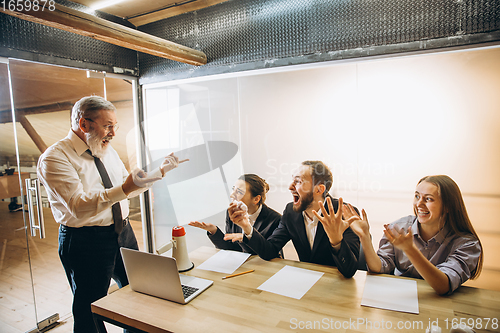 Image of Angry boss with megaphone screaming at employees in office, scared and annoyed colleagues listening at the table