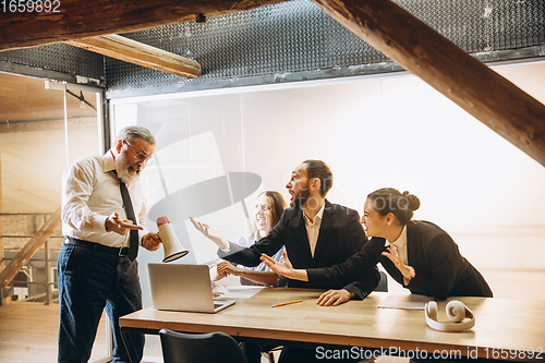 Image of Angry boss with megaphone screaming at employees in office, scared and annoyed colleagues listening at the table