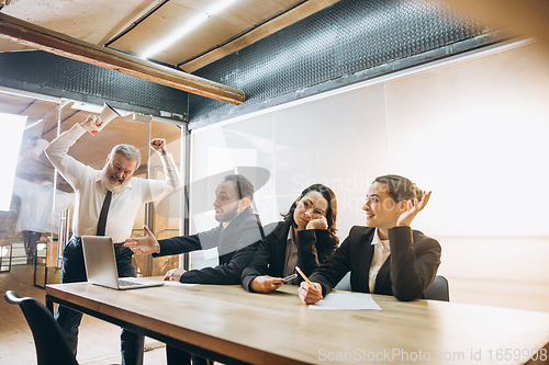 Image of Angry boss with megaphone screaming at employees in office, scared and annoyed colleagues listening at the table