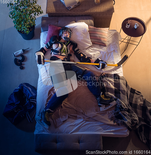 Image of Top view of young professional hockey player sleeping at his bedroom in sportwear with equipment