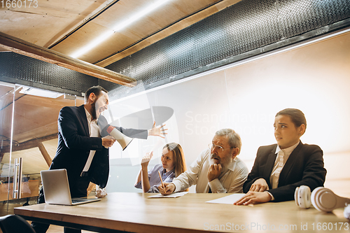 Image of Angry boss with megaphone screaming at employees in office, scared and annoyed colleagues listening at the table