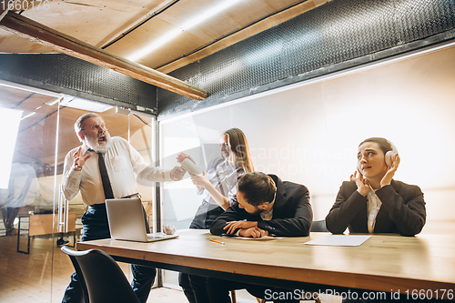 Image of Angry boss with megaphone screaming at employees in office, scared and annoyed colleagues listening at the table