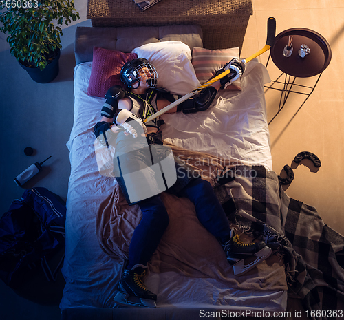 Image of Top view of young professional hockey player sleeping at his bedroom in sportwear with equipment