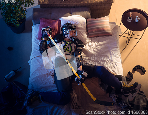 Image of Top view of young professional hockey player sleeping at his bedroom in sportwear with equipment