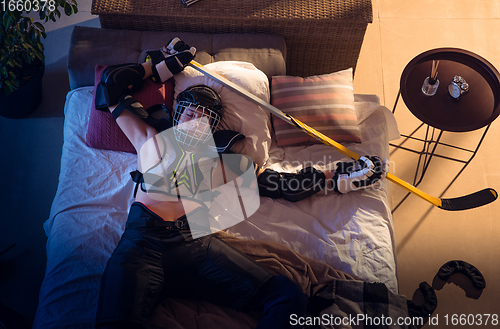 Image of Top view of young professional hockey player sleeping at his bedroom in sportwear with equipment