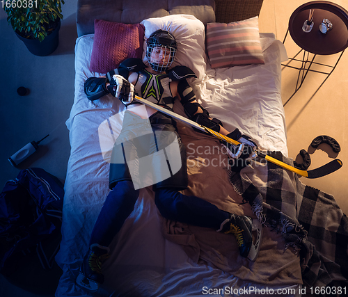 Image of Top view of young professional hockey player sleeping at his bedroom in sportwear with equipment