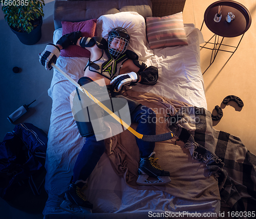 Image of Top view of young professional hockey player sleeping at his bedroom in sportwear with equipment