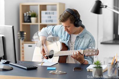 Image of man in headphones playing guitar at home