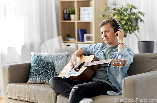 Image of man in headphones playing guitar at home