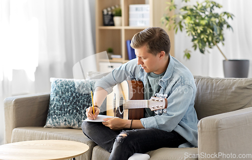 Image of man with guitar writing to music book at home