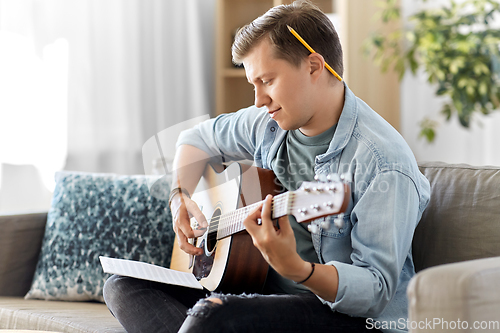 Image of young man with music book playing guitar at home