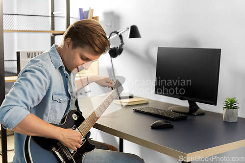 Image of young man with computer playing guitar at home