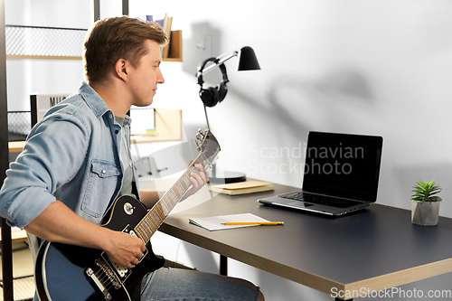 Image of young man with laptop playing guitar at home