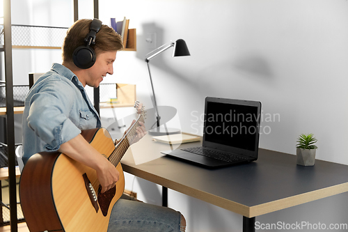 Image of man in headphones playing guitar at home