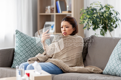 Image of sick asian woman with smartphone at home