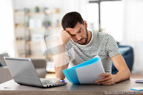 Image of man with papers and laptop working at home office