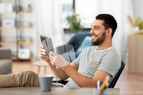 Image of man with tablet pc resting feet on table at home