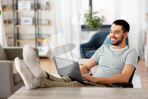 Image of man with laptop resting feet on table at home