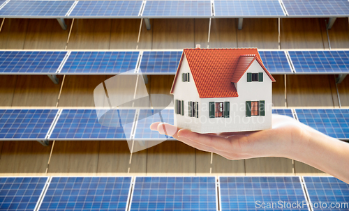 Image of hand holding house model over solar panels