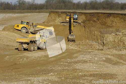 Image of Yellow dump trucks and excavator are working in gravel pit