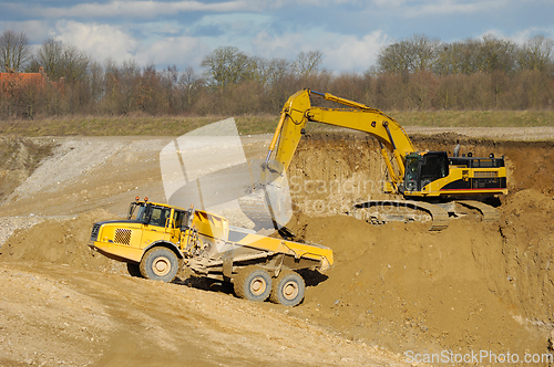 Image of Yellow dump trucks and excavator are working in gravel pit