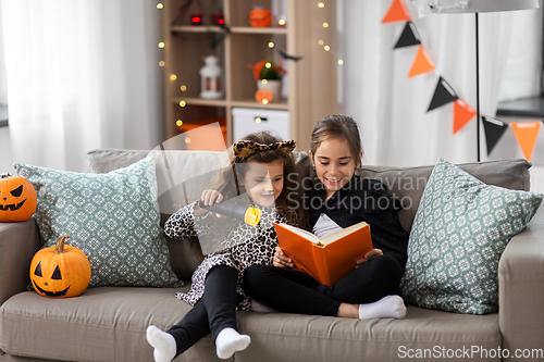 Image of girls in halloween costumes reading book at home