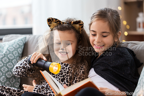 Image of girls in halloween costumes reading book at home