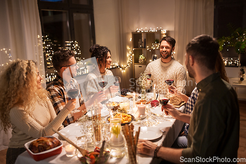 Image of happy friends drinking red wine at christmas party