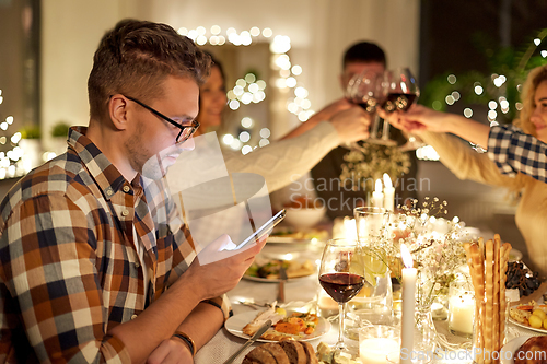 Image of man with smartphone at dinner party with friends