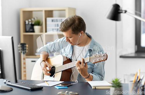 Image of man with earphones and smartphone playing guitar