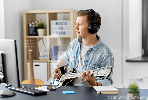 Image of man in headphones playing bass guitar at home