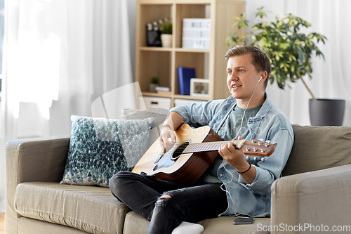 Image of man with guitar, earphones and smartphone at home