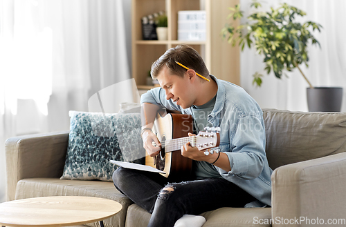 Image of young man with music book playing guitar at home