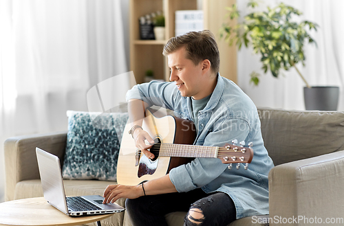 Image of young man with laptop playing guitar at home