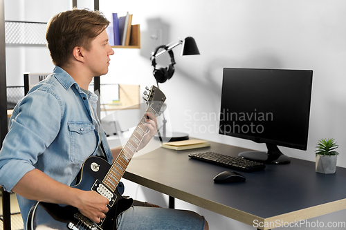 Image of young man with computer playing guitar at home