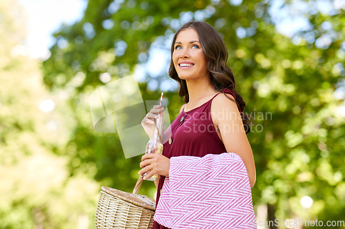 Image of happy woman with picnic basket and drink at park