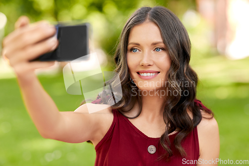 Image of happy woman with smartphone taking selfie at park