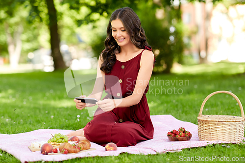 Image of happy woman with smartphone on picnic at park